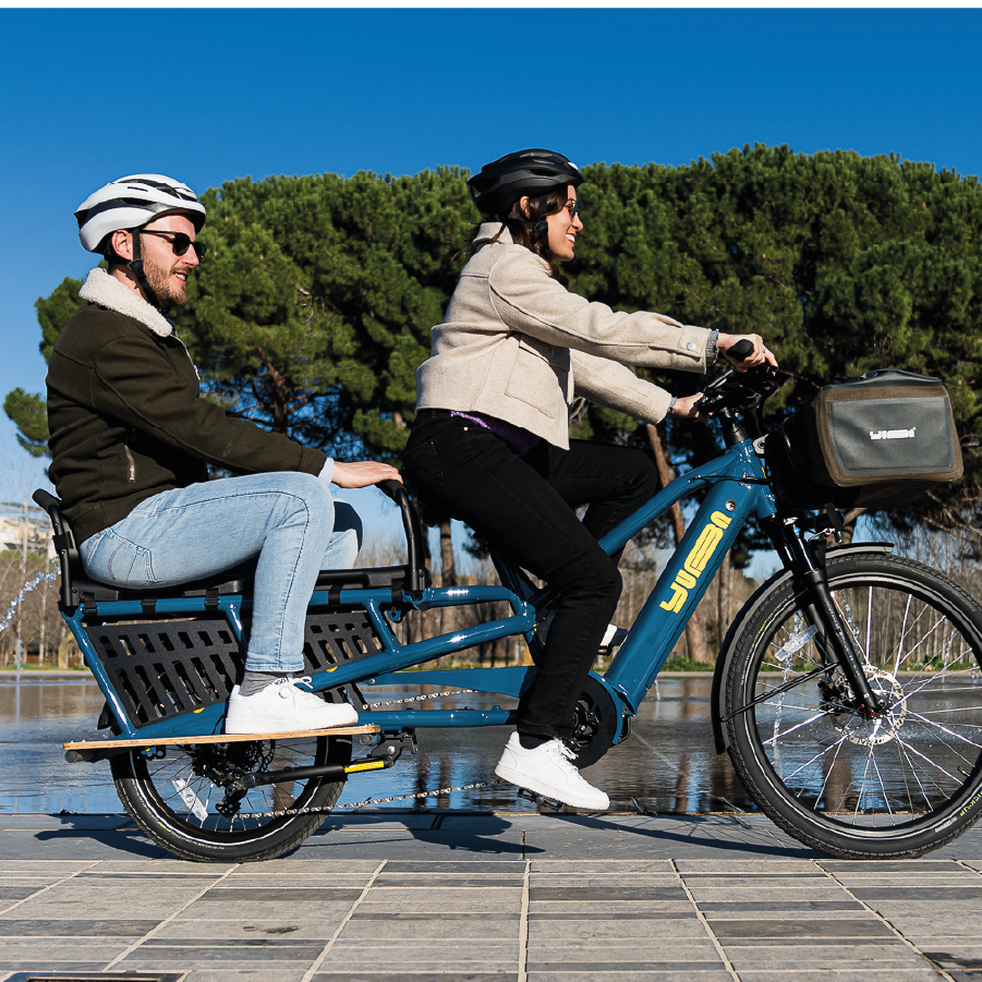 Ein Mann und eine Frau fahren zusammen mit Yuba Spicy curry in Farbe true blue durch die Stadt.