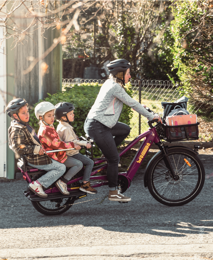Eine Frau transportiert ihre Kinder mit Yuba Spicy Curry in very berry durch die Stadt.